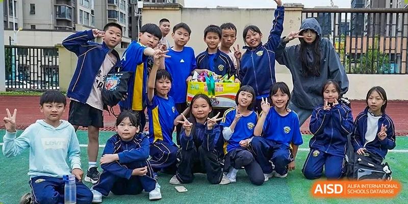 A large group of primary students smile and pose together behind a box of prizes on the field at Beijing International Bilingual Academy Guiyang.