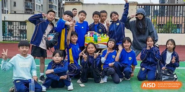 A large group of primary students smile and pose together behind a box of prizes on the field at Beijing International Bilingual Academy Guiyang.