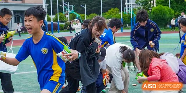 A teacher laughs while participating in a fun snack-grabbing game with students on the turf field at Beijing International Bilingual Academy Guiyang.