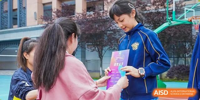 A student receives a bright purple award certificate from a teacher during a recognition ceremony at Beijing International Bilingual Academy Guiyang.