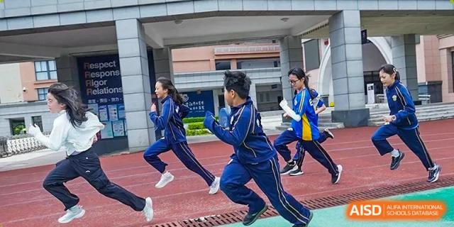 Two students in blue tracksuits race side-by-side down the running track during a physical education class at Beijing International Bilingual Academy Guiyang.