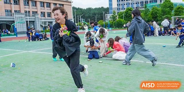 A woman runs joyfully across the green field while clutching prizes during a community event at Beijing International Bilingual Academy Guiyang.