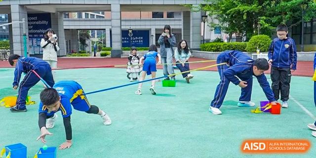 A student jumps over a blue hurdle on the green outdoor court during a sports competition at Beijing International Bilingual Academy Guiyang.