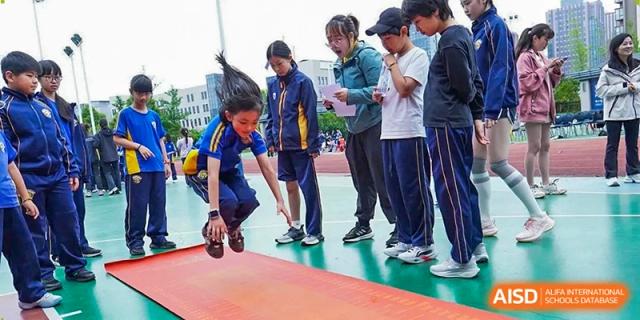 A student performs a long jump on a red mat while classmates watch and record the results at Beijing International Bilingual Academy Guiyang.