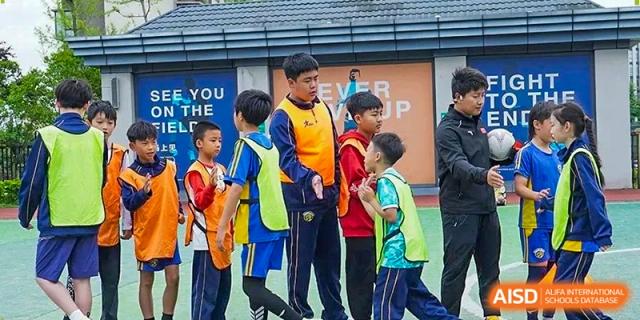 A teacher in an orange and blue vest instructs a group of young students on the sports court at Beijing International Bilingual Academy Guiyang.