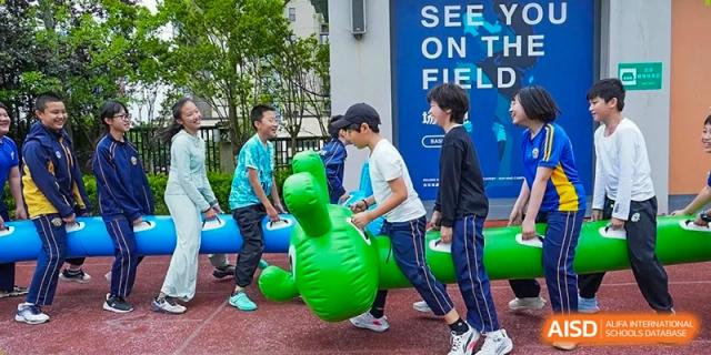 Two boys in blue shirts play with an inflatable green toy on a red track during a field day event at Beijing International Bilingual Academy Guiyang.