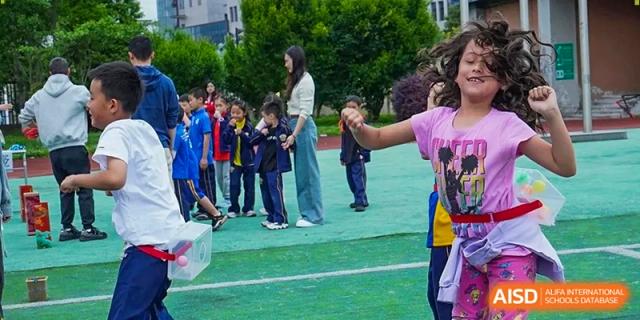 A teacher in a white blouse leads a line of young students in blue uniforms across the outdoor turf at Beijing International Bilingual Academy Guiyang.