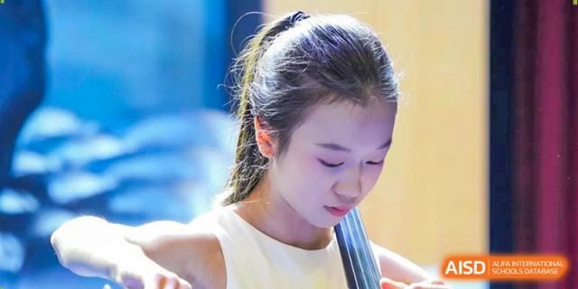 A young girl looks down with concentration while playing the cello during a school concert at Beijing International Bilingual Academy Guiyang.