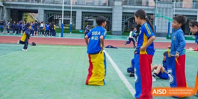 A student in a blue "BIBA" shirt participates in a yellow sack race on the green sports field at Beijing International Bilingual Academy Guiyang.