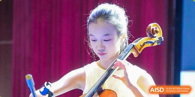 A student in a white dress plays the cello, highlighting the school's performing arts program at Beijing International Bilingual Academy Guiyang.
