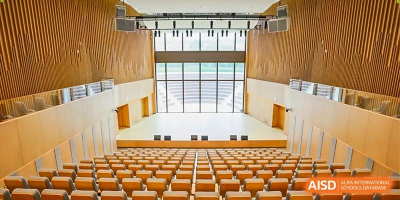 A high-angle view of a large, modern school auditorium with tiered wooden seating facing a bright stage at Benenden Bilingual School Guangzhou