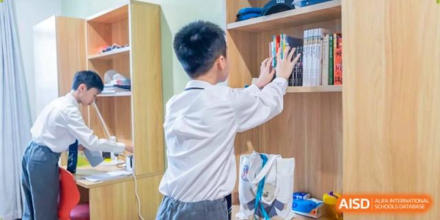 A young male student in a white shirt organizes his belongings in a wooden locker inside a school dorm at Benenden Bilingual School Guangzhou
