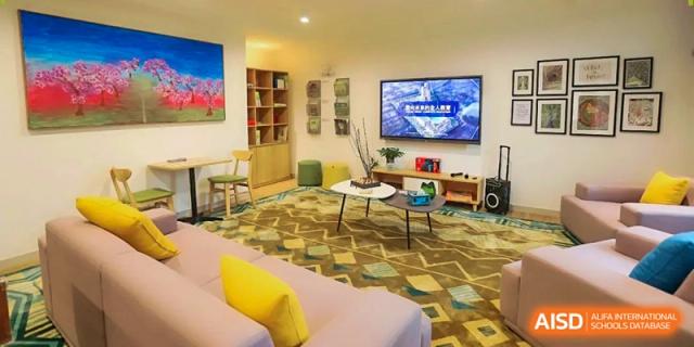 A cozy student lounge area featuring a large television, comfortable sofas, and a patterned green rug at Benenden Bilingual School Guangzhou