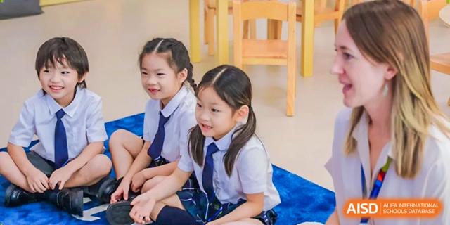 Two young female students in white shirts and blue ties sit together during a classroom activity at Benenden Bilingual School Guangzhou