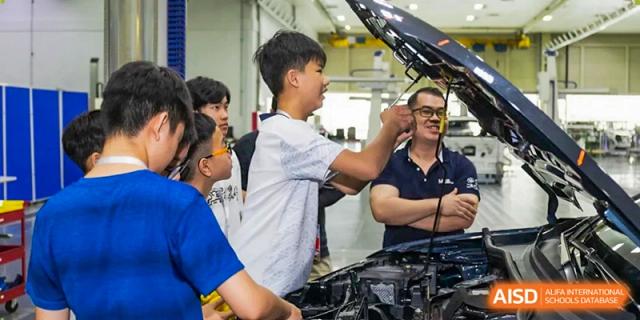 A student works under the hood of a car with an instructor during a practical automotive workshop at Benenden Bilingual School Guangzhou