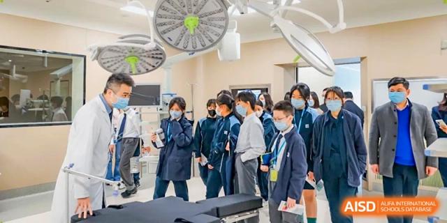 A group of students in lab coats gather around a specialized piece of equipment during a medical science class at Benenden Bilingual School Guangzhou