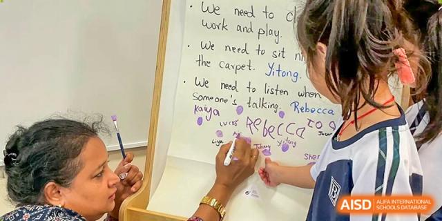 A close-up of a teacher's hand writing collaborative notes on a large white flip chart during a lesson at Benenden Bilingual School Guangzhou