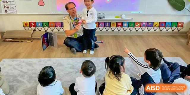 A teacher sits on a rug while engaging with a small group of young children during a classroom activity at Benenden Bilingual School Guangzhou