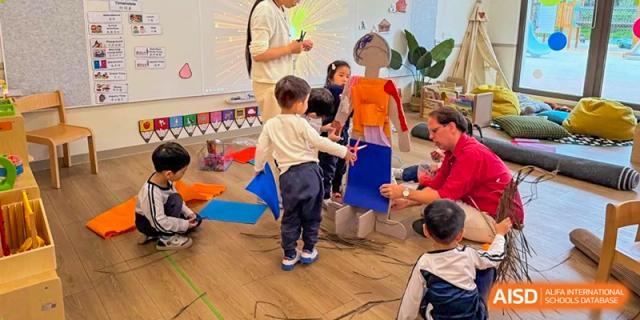 Young students and teachers collaborate on a creative project using large cutouts and blue paper on a classroom floor at Benenden Bilingual School Guangzhou
