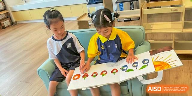 A young student points to colorful fruit illustrations in a large picture book during a group reading session at Benenden Bilingual School Guangzhou