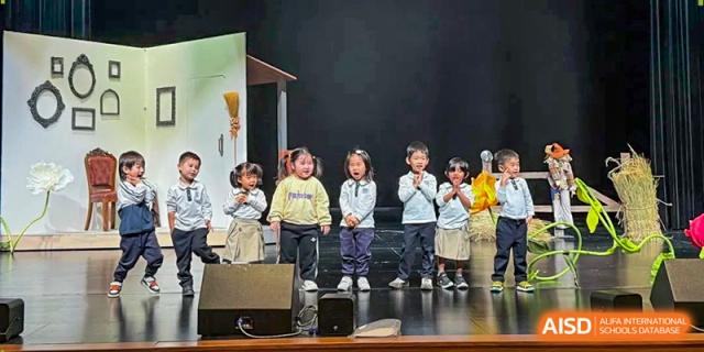 Four young children stand on a small stage and perform a song together for their classmates at Benenden Bilingual School Guangzhou