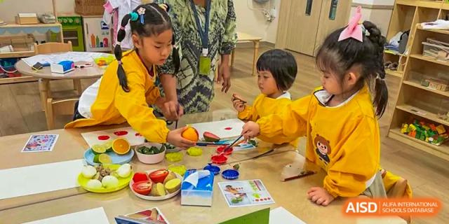 A teacher helps a group of students prepare healthy snacks with fresh fruits and vegetables at a classroom table at Benenden Bilingual School Guangzhou