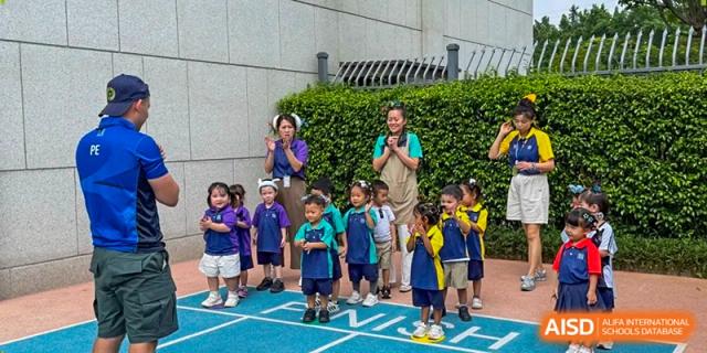 A large group of students and teachers gather outdoors on a blue court for a group activity or celebration at Benenden Bilingual School Guangzhou
