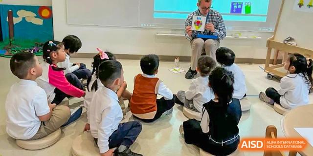 A small group of students sits on the floor and listens attentively to a teacher during an indoor classroom lesson at Benenden Bilingual School Guangzhou