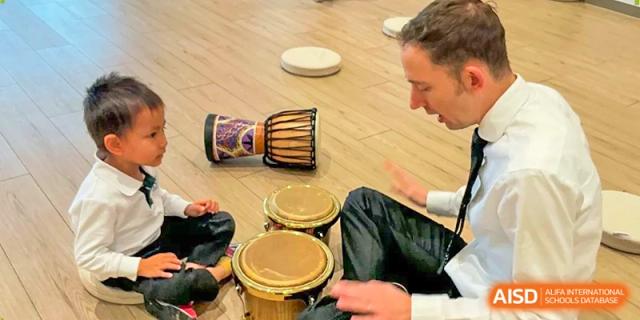 A close-up view of hands playing small drums during an interactive music and rhythm class for young learners at Benenden Bilingual School Guangzhou