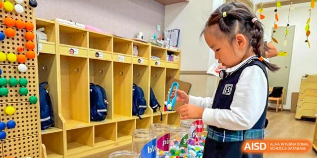 A young student focuses on a task near a row of organized wooden cubbies and storage bins in a tidy classroom at Benenden Bilingual School Guangzhou