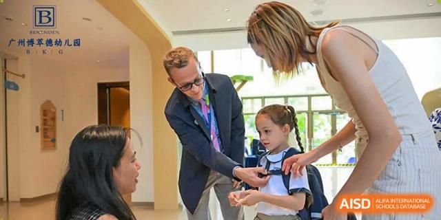 A teacher in a suit jacket helps a young student adjust her school bag or equipment during a transition period at Benenden Bilingual School Guangzhou