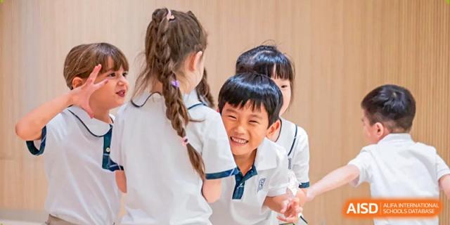 A group of young students share a joyful moment and laugh together during a fun indoor school activity at Benenden Bilingual School Guangzhou