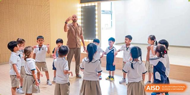 A teacher leads a group of young students in a movement-based activity or dance in front of a mirror at Benenden Bilingual School Guangzhou