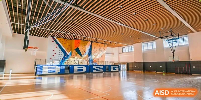 A spacious indoor gymnasium featuring polished wooden floors and a large colorful climbing wall at Benenden Bilingual School Guangzhou