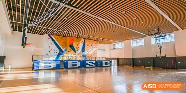 A spacious indoor gymnasium featuring polished wooden floors and a large colorful climbing wall at Benenden Bilingual School Guangzhou