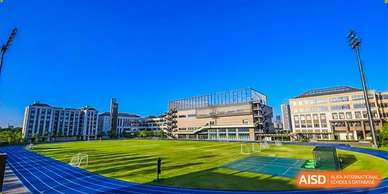 An outdoor athletic field with vibrant green turf and a blue running track under a clear blue sky at Benenden Bilingual School Guangzhou