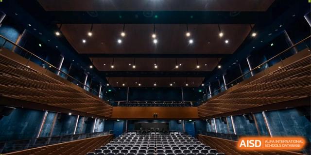 A wide-angle view of a professional school auditorium with rows of grey seating and modern stage lighting at Benenden Bilingual School Guangzhou