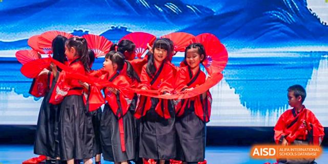 A group of female students in traditional red and black attire perform a fan dance on stage at Benenden Bilingual School Guangzhou