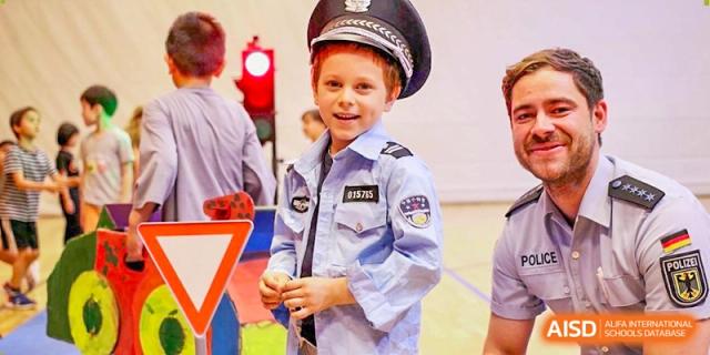 A young student dressed in a miniature police officer uniform smiles during a school role-playing activity. Deutsche Botschaftsschule Peking