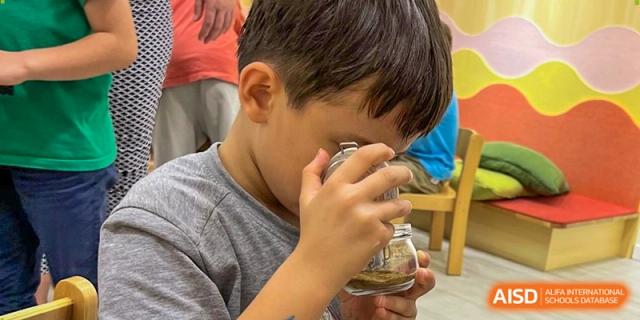 A young student looks closely through a magnifying glass at a small specimen jar during a science discovery. Deutsche Botschaftsschule Peking