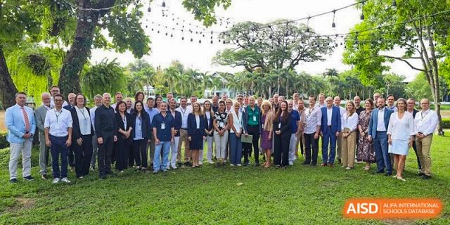A large group of staff and faculty members pose together for a formal group photo on a green lawn outdoors. Deutsche Botschaftsschule Peking