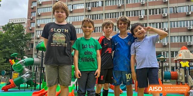 Five young boys in colorful t-shirts stand together smiling for a group photo on the school playground. Deutsche Botschaftsschule Peking