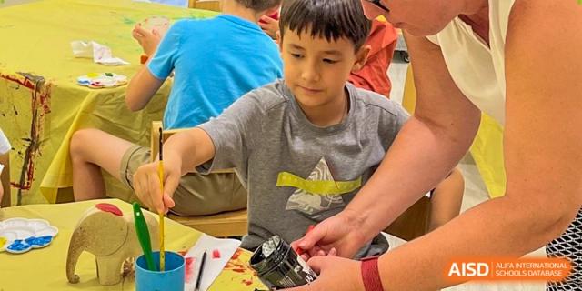 A student carefully dips a paintbrush into a jar of paint while working on a craft project in the classroom. Deutsche Botschaftsschule Peking