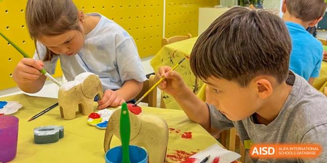 A child focuses intently on painting a small elephant sculpture with bright red and blue colors. Deutsche Botschaftsschule Peking