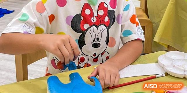 Close-up of a student in a Minnie Mouse shirt using blue clay to sculpt a creative figure during playtime. Deutsche Botschaftsschule Peking