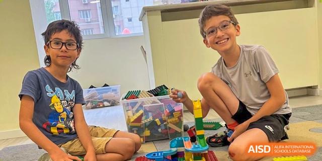 Two boys smile brightly while building a complex marble run and tower using colorful plastic blocks. Deutsche Botschaftsschule Peking