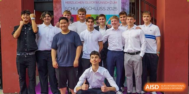 A group of male graduates in formal white shirts smile together in front of a celebratory banner. Deutsche Botschaftsschule Peking