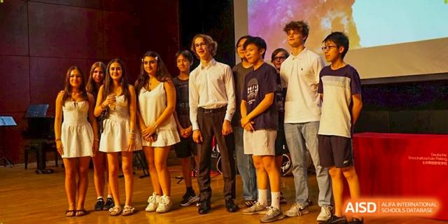 A large group of students in formal attire stand together on a stage for a final commemorative photo. Deutsche Botschaftsschule Peking