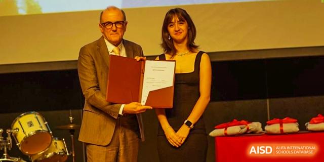 A student in a black dress receives her diploma and poses for a photo with a faculty member on stage. Deutsche Botschaftsschule Peking