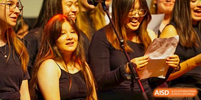 A close-up of a student singing or speaking into a microphone during a musical performance on stage. Deutsche Botschaftsschule Peking